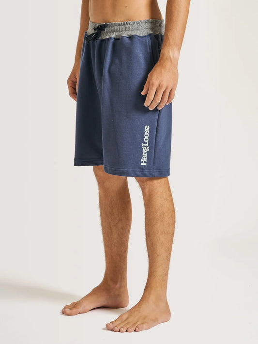 Modelo vestindo a bermuda moletom azul marinho da Hang Loose. A peça possui cós cinza e cordão para ajuste na cor preta.
