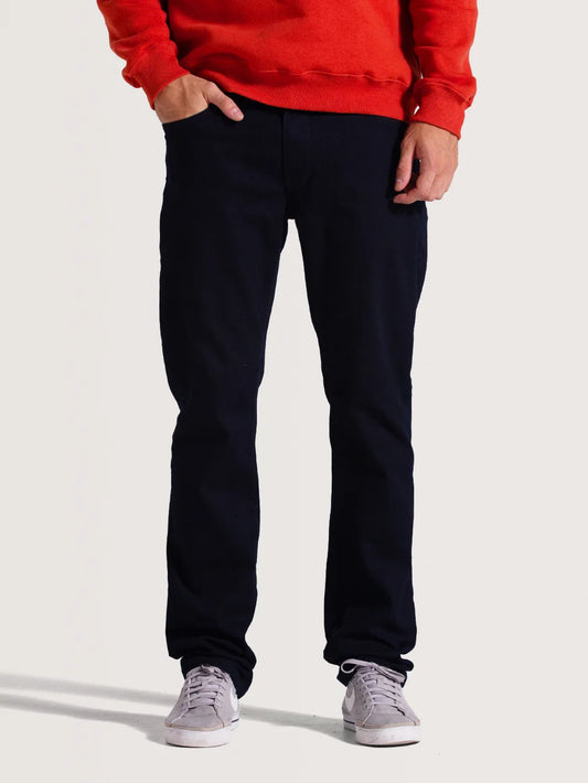 Homem vestindo calça jeans preta. A roupa é ajustada ao corpo e modelo combina a peça com tênis lilás e moletom vermelho.