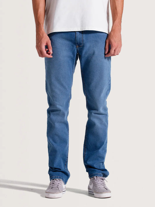 Modelo vestindo calça jeans slim fit. Homem combina a peça com camiseta branca básica e tênis lilás.