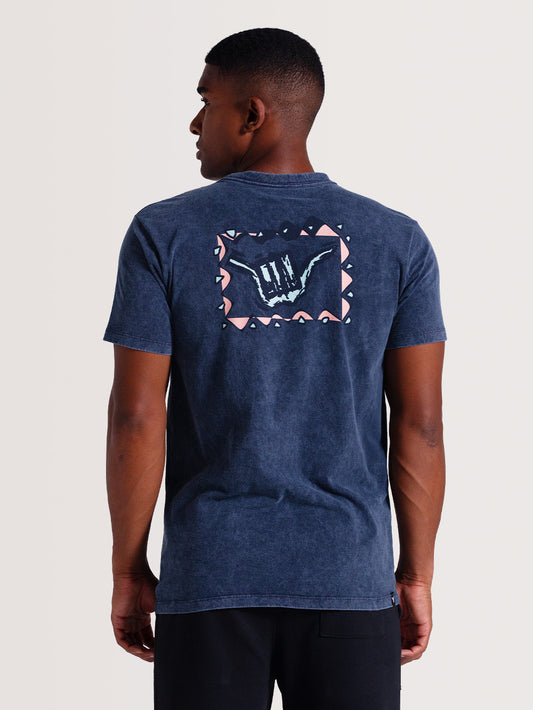Homem de costas vestindo camiseta azul manga longa com design minimalista de pequenas ondas brancas no ombro, capturado em um fundo neutro.