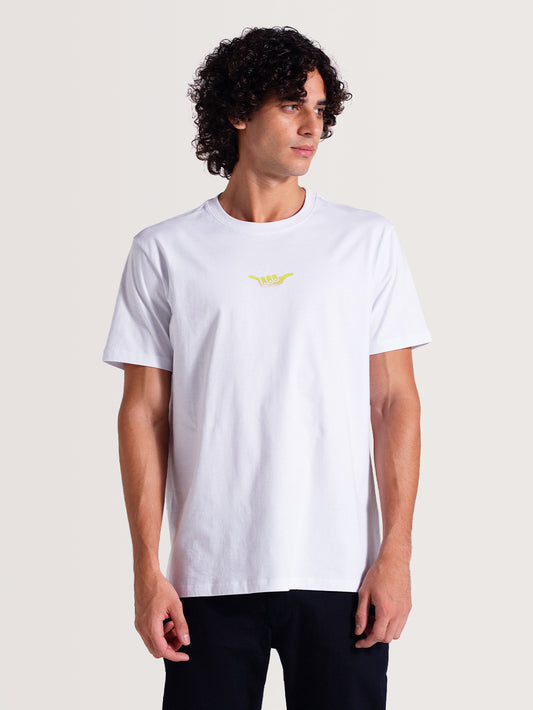 Homem vestindo camiseta básica branca manga curta com pequeno símbolo "Hang Loose" em amarelo no centro do peito, combinando com calça preta.