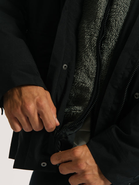 Mãos ajustando o zíper de uma jaqueta pesada preta 3 em 1, mostrando o forro interno de lã cinza, ideal para proteção térmica e conforto em clima frio.