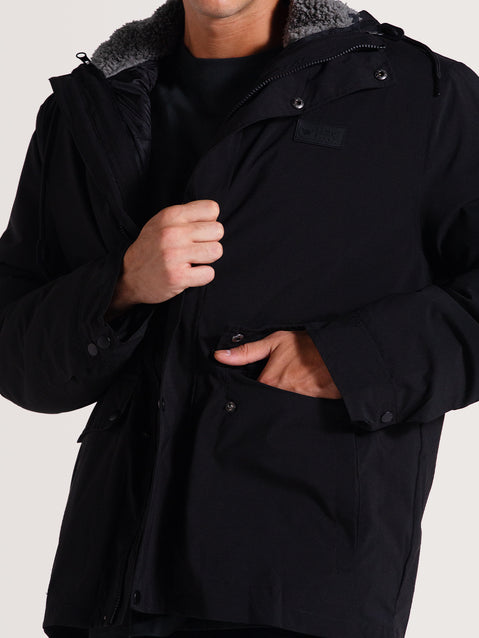 Homem ajustando uma jaqueta pesada preta 3 em 1, com capuz e forro de lã visível, além de bolsos frontais com botões, mantendo um estilo funcional.