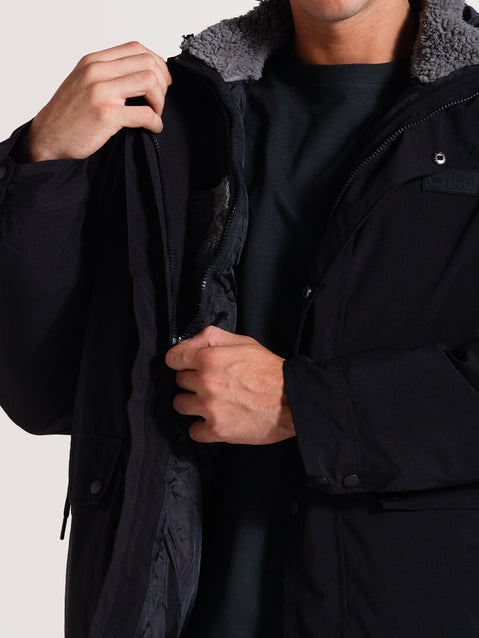 Homem ajustando o zíper de uma jaqueta pesada preta 3 em 1, com forro interno de lã cinza visível, ideal para manter o conforto térmico.