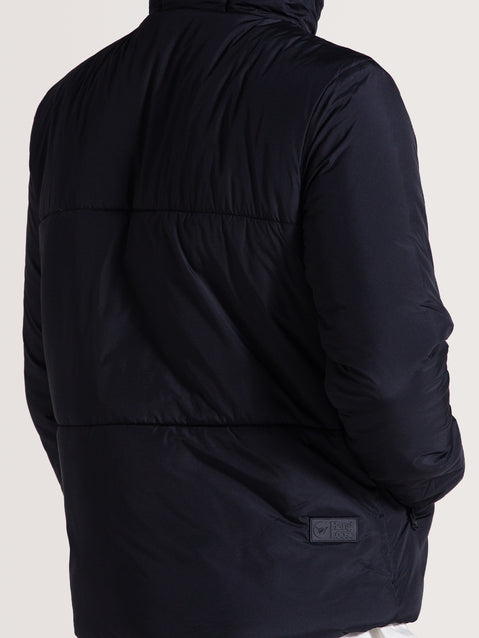 Homem de costas usando jaqueta puffer preta com acabamento liso, costuras horizontais e detalhe de etiqueta próxima à barra lateral.