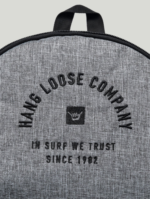 Detalhe da Mochila Hang Loose com tecido cinza texturizado. O logo traz a inscrição "Hang Loose Company" e "In Surf We Trust Since 1982".