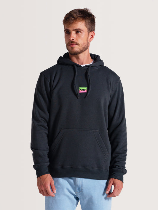 Homem vestindo um moletom canguru cinza com capuz, bolso frontal e cordões ajustáveis. Patch colorido no peito e visual casual.