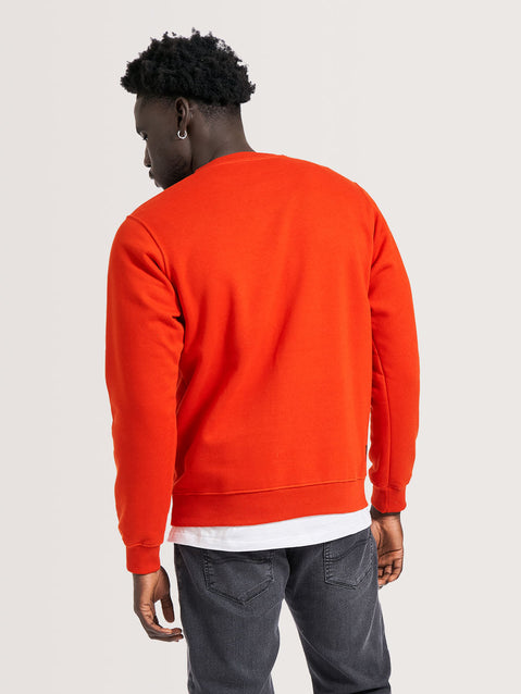 Homem usando moletom vermelho careca com gola redonda, modelagem regular e tecido liso. Combina com camiseta branca e jeans cinza casual.