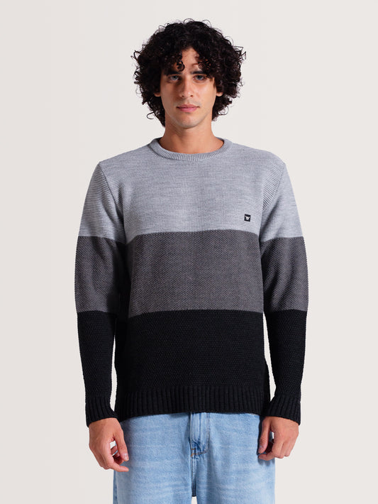 Homem vestindo tricot cinza com listras em tons de cinza e preto. Modelo de gola redonda e detalhe de patch no peito. Fundo claro.