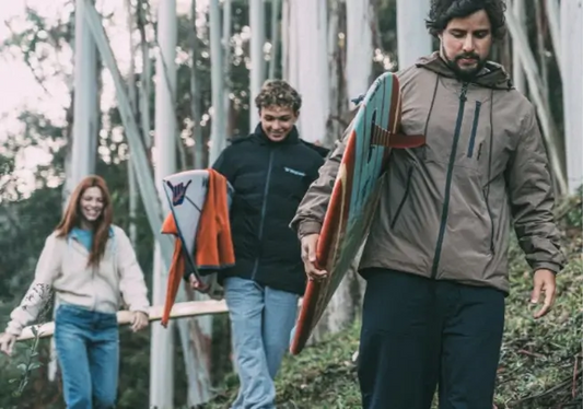Surfistas carregando pranchas em roupas estilosas em meio a área de mato.