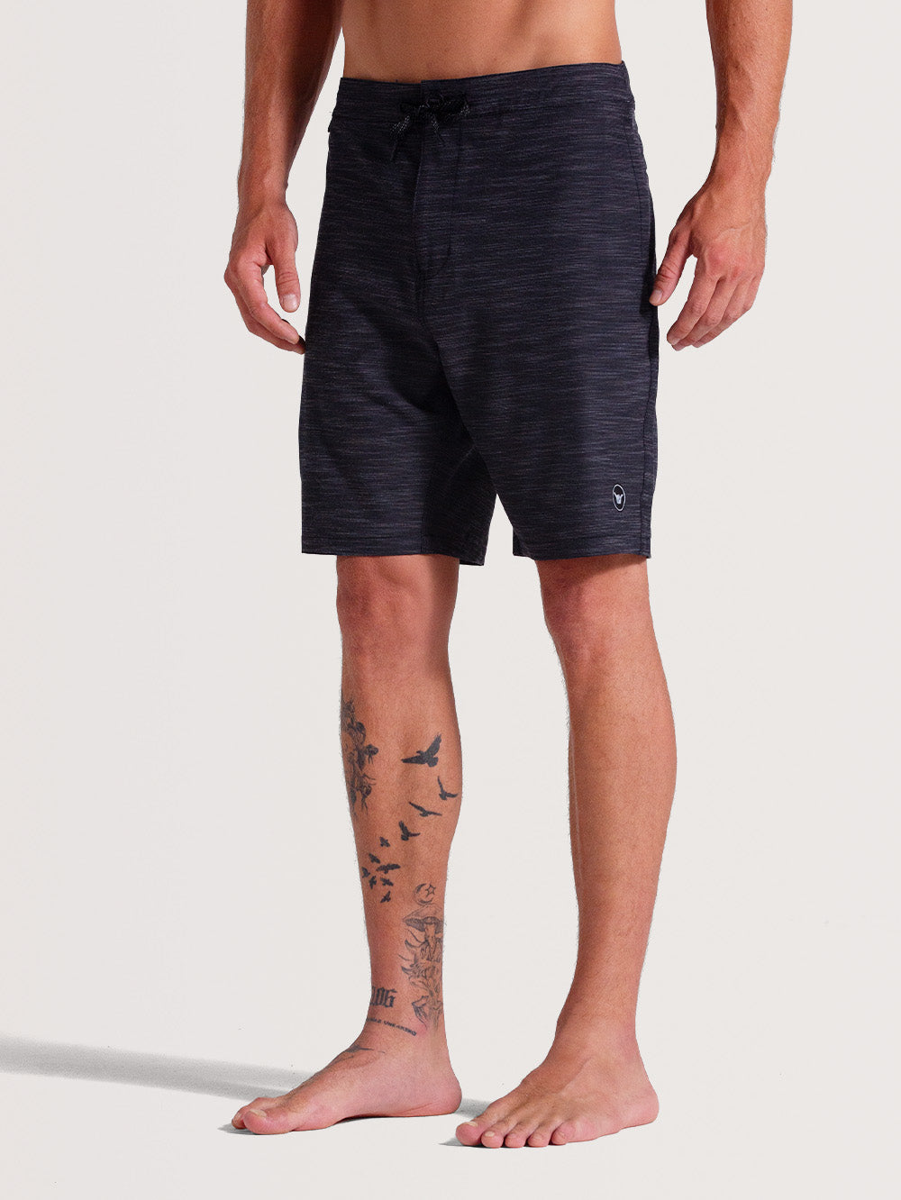 Homem vestindo bermuda híbrida 19 polegadas preto, estilo casual, com estampa discreta em tom mesclado e logo minimalista próximo à barra. Peça confortável e versátil.
