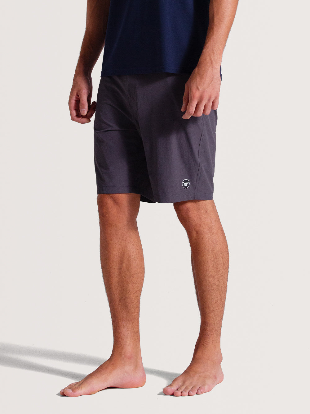 Homem vestindo bermuda híbrida preta com tecido leve e ajuste confortável, logo discreto em branco próximo à barra, combinada com camiseta azul marinho.