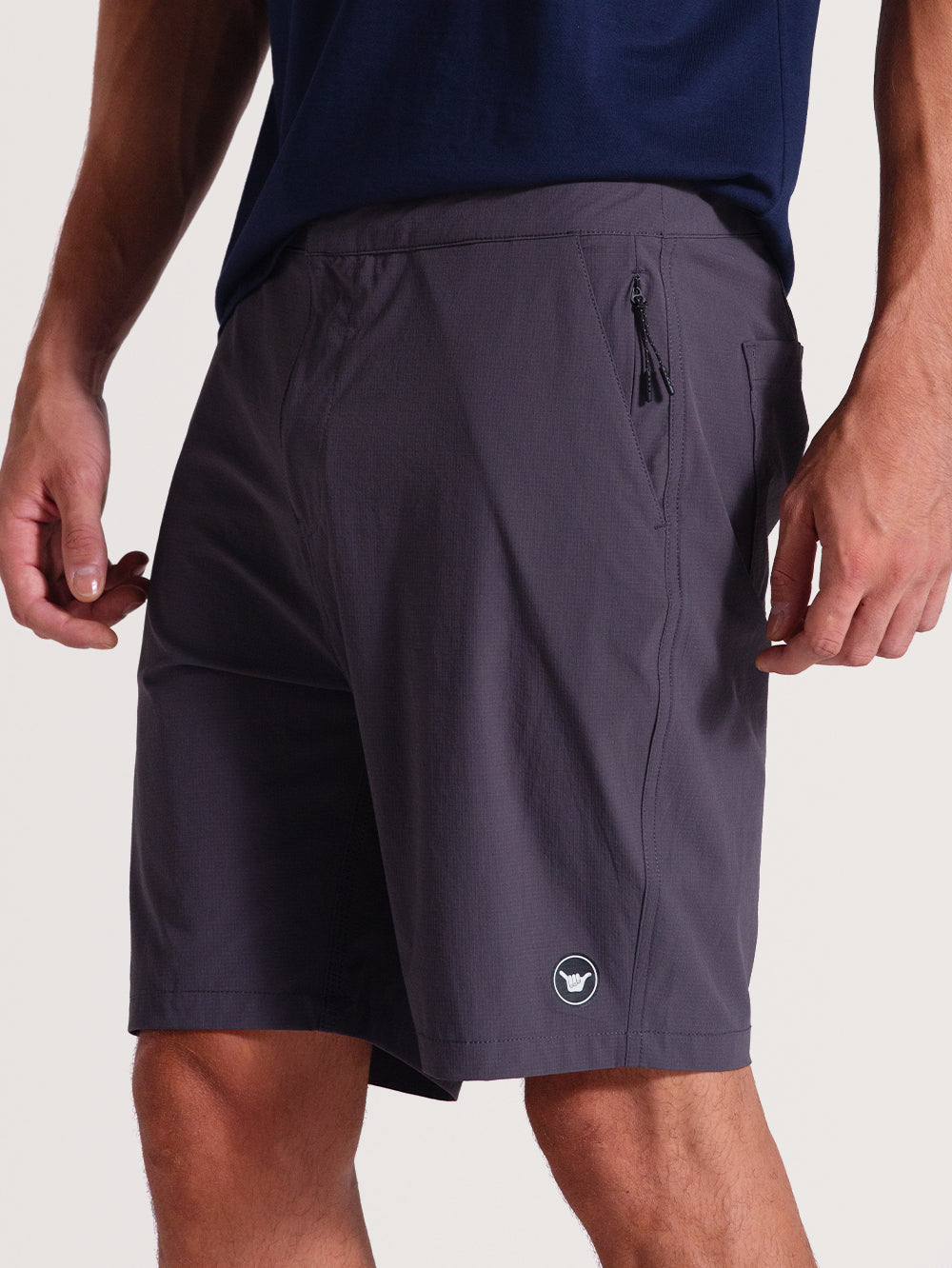 Bermuda híbrida preta com tecido leve texturizado, bolso lateral com zíper e logo discreto branco próximo à barra. Estilo funcional e casual.