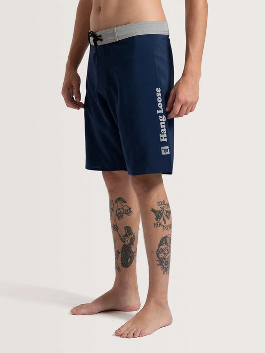 Modelo vestindo boardshort azul marinho. O item possui cós na cor cinza, cadarço para ajuste e nome da marca na lateral.