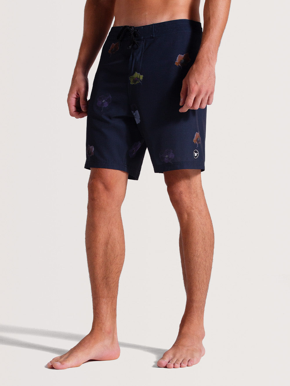 Homem vestindo boardshorts 18 polegadas cinza com estampa minimalista de flores, ajuste por cordão preto na cintura. Design moderno e confortável.