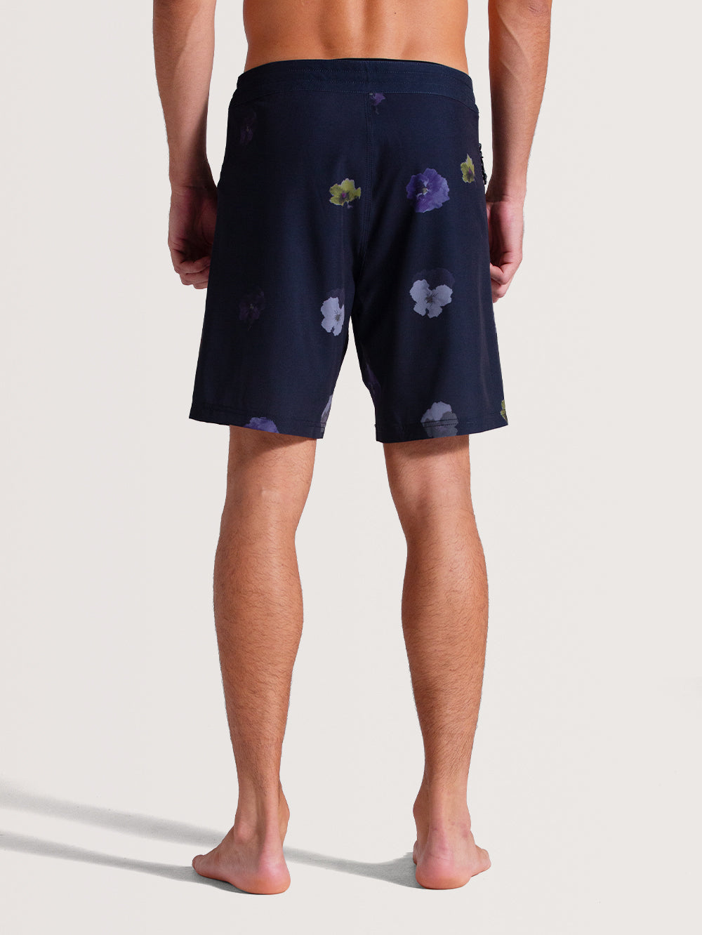 Homem de costas vestindo boardshorts 18 polegadas cinza com estampa floral discreta em tons escuros, corte acima do joelho e tecido leve, ideal para ocasiões casuais.