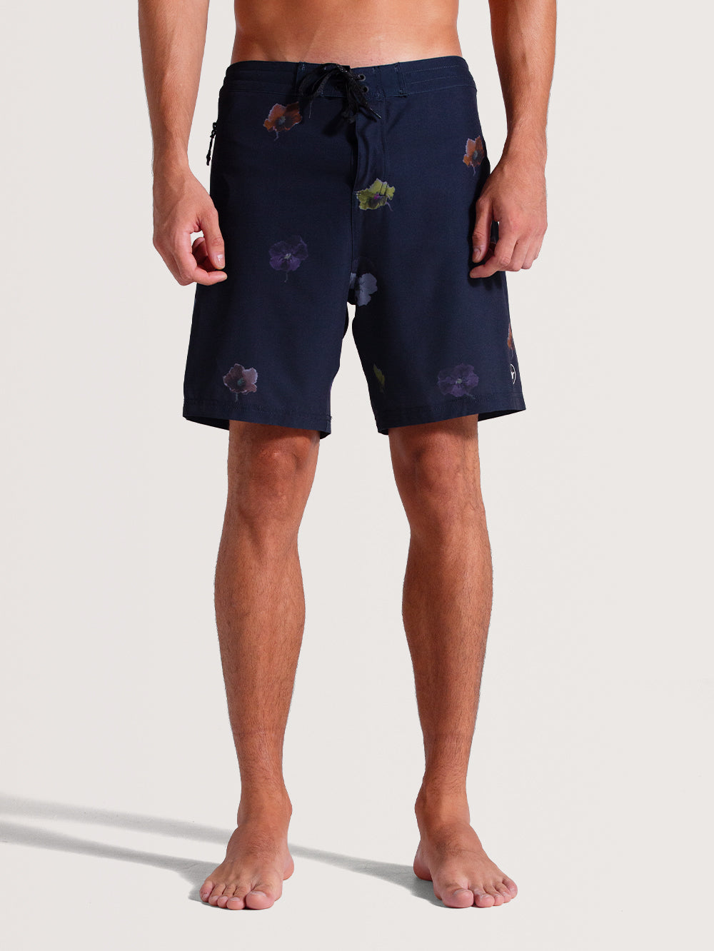 Homem vestindo boardshorts 18 polegadas cinza com estampa floral discreta em tons coloridos, ajuste na cintura com cordão preto. Design casual e funcional.