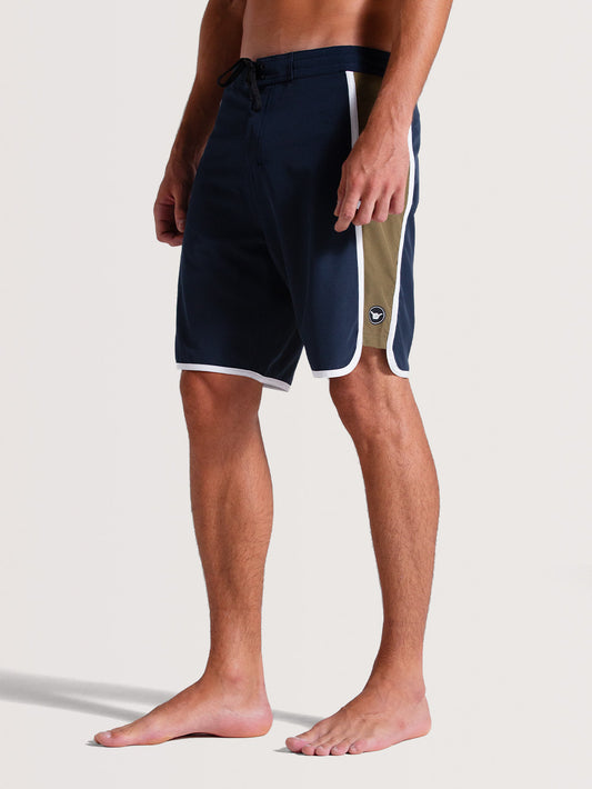 Boardshorts 19 polegadas azul-marinho com detalhes laterais em branco e bege, cós ajustável com cordão preto, ideal para atividades aquáticas.