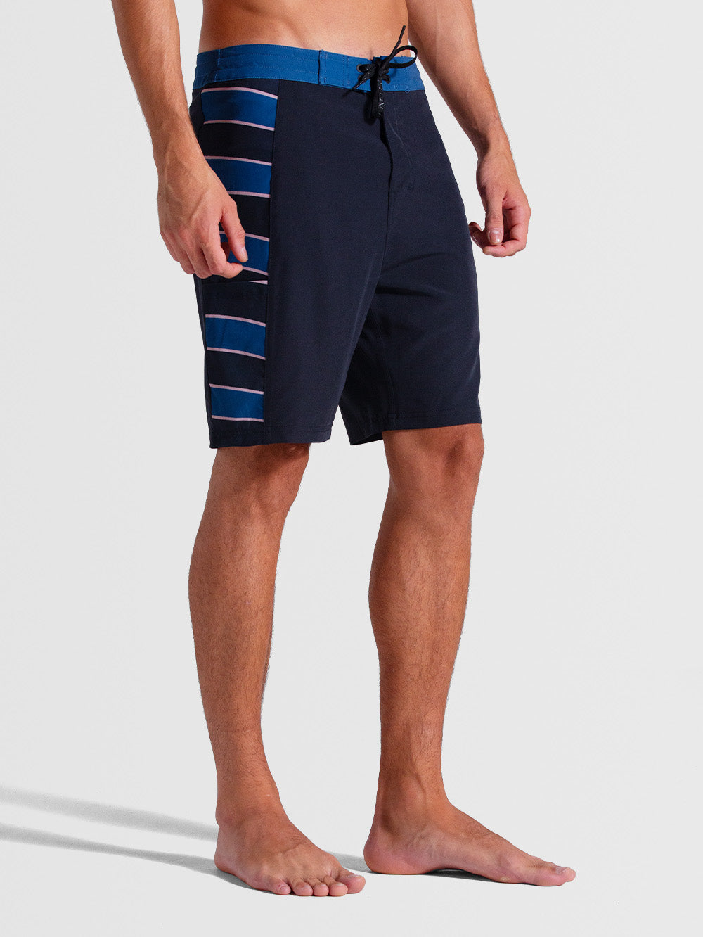 Homem vestindo boardshorts 19 polegadas chumbo com detalhes listrados em azul na lateral, cós azul contrastante e ajuste com cordão preto. Estilo esportivo e moderno.