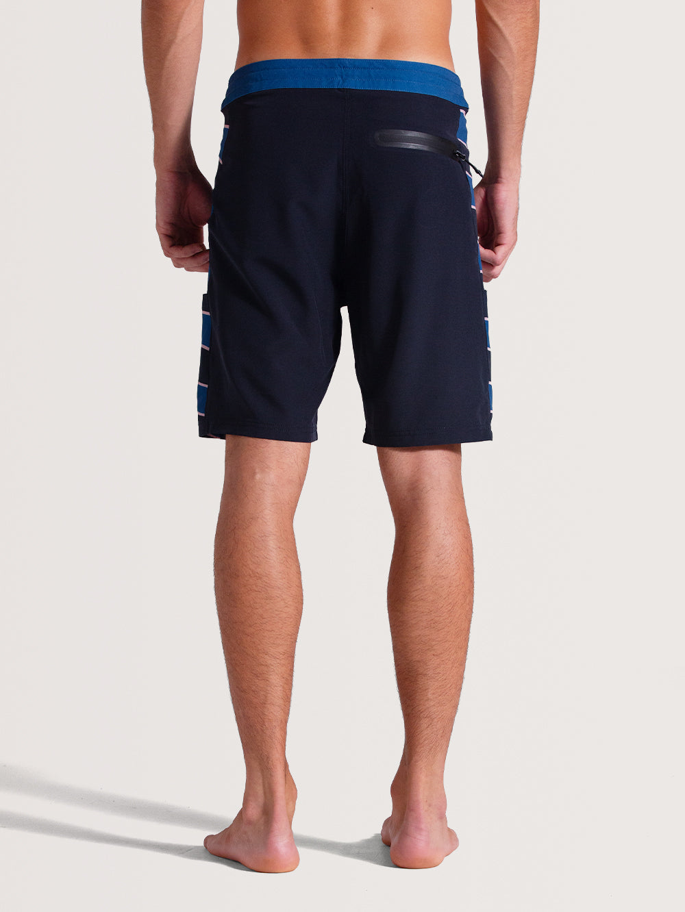 Homem de costas vestindo boardshorts 19 polegadas chumbo com cós azul contrastante, detalhe de bolso com zíper na lateral e listras azuis nas laterais.