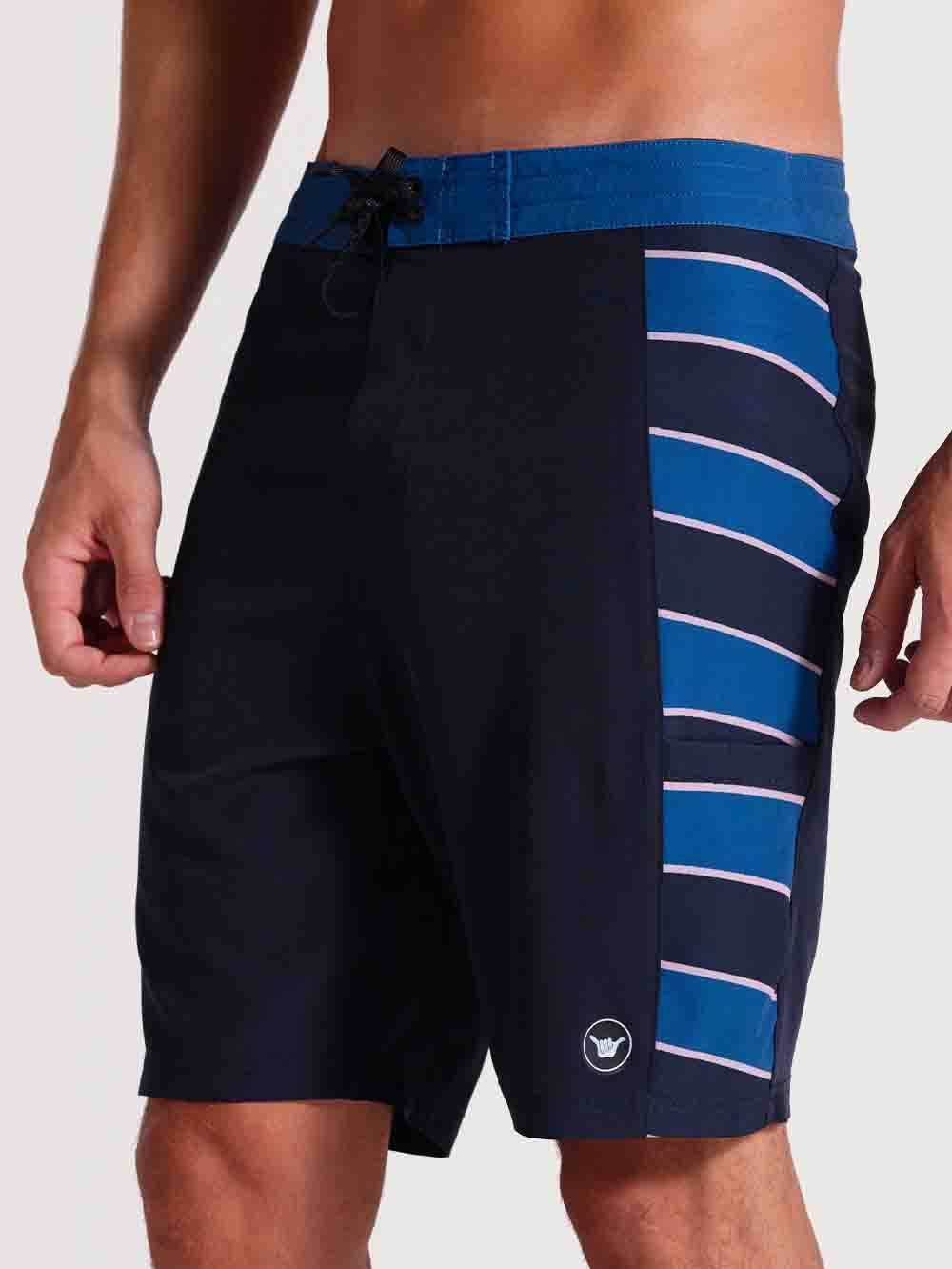 Boardshorts 19 polegadas chumbo com cós azul, listras laterais em azul e branco, ajuste por cordão preto e logo discreto na perna esquerda.