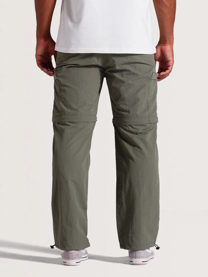 Homem de costas vestindo calça híbrida 2 em 1 verde, com zíper para conversão em bermuda na altura dos joelhos e ajuste por cordão nas barras.