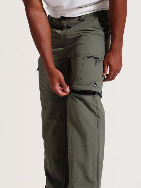 Homem ajustando o zíper da calça híbrida 2 em 1 verde-oliva, destacando sua funcionalidade para conversão em bermuda. Peça leve e prática, ideal para aventuras.
