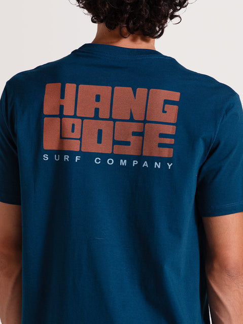 Camiseta azul manga curta com estampa grande "Hang Loose Surf Company" em laranja e branco nas costas. Estilo descontraído e casual.