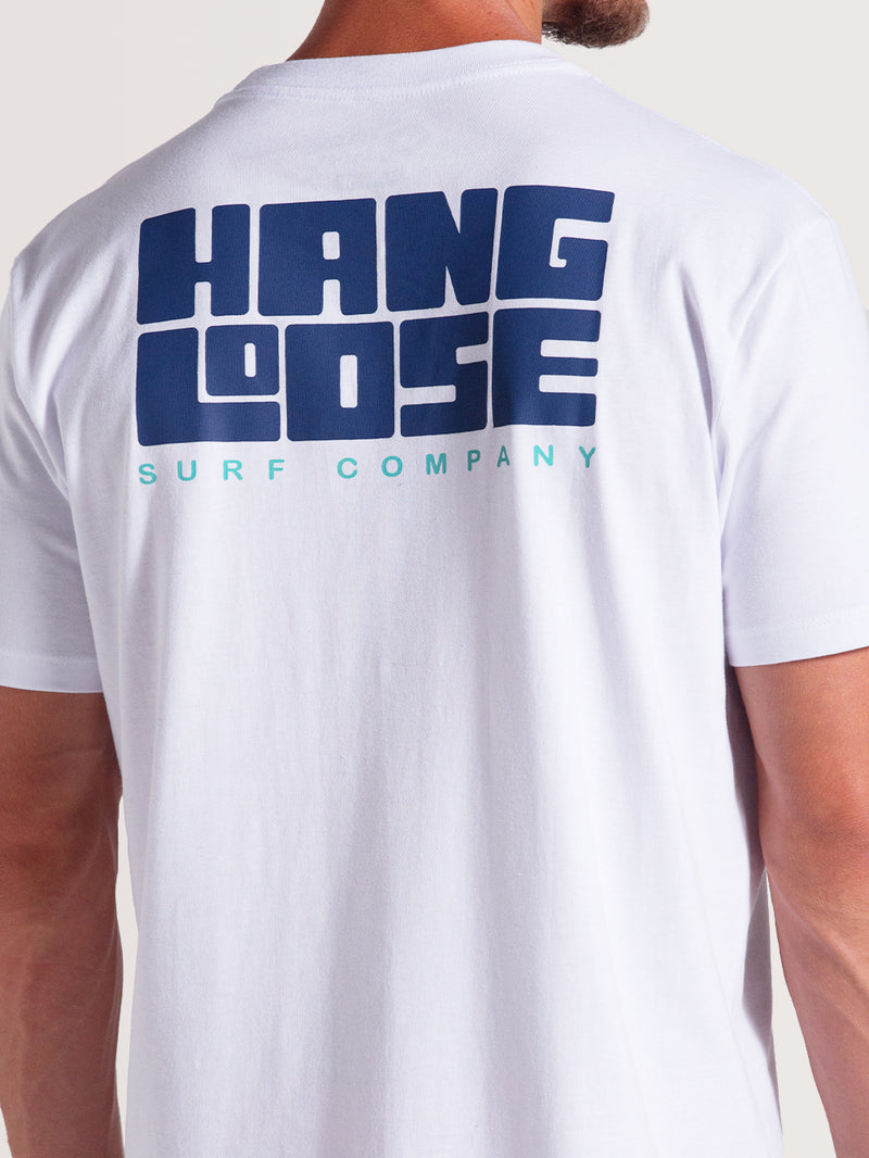 Homem vestindo camiseta branca manga curta com estampa traseira grande em azul escuro "Hang Loose" e texto menor "Surf Company" em azul claro.