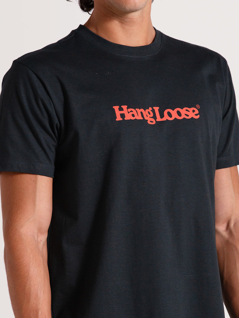 Homem vestindo camiseta preta algodão manga curta com gola redonda e logo "Hang Loose" vermelho no peito.