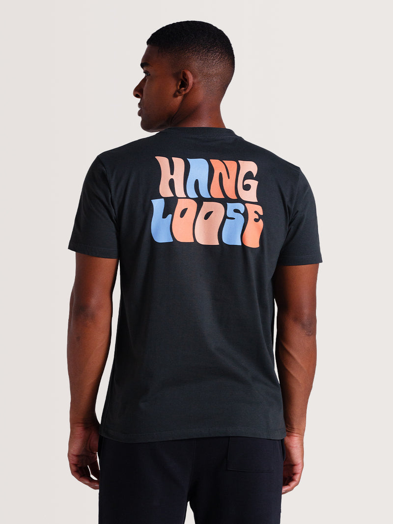 Homem vestindo camiseta cinza básica manga curta com estampa traseira "Hang Loose" em letras grandes nas cores azul e laranja pastel.