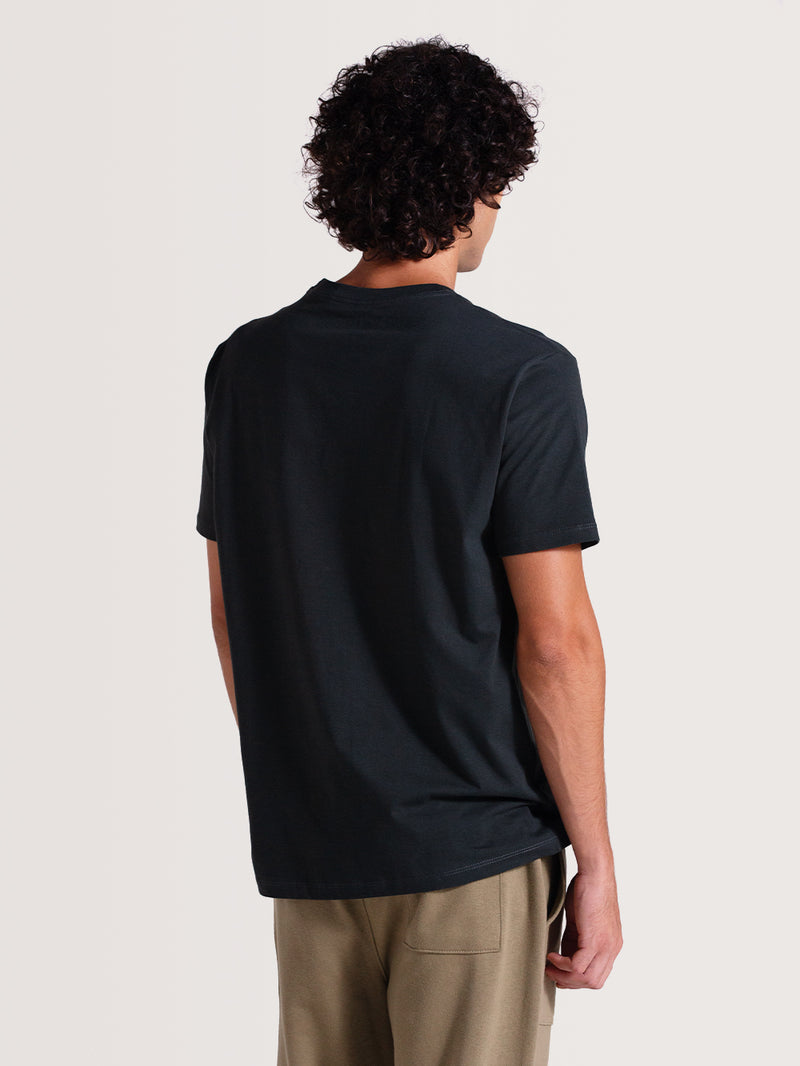 Homem vestindo camiseta cinza chumbo manga curta, com design simples e sem estampas visíveis na parte de trás, combinada com calça bege casual.