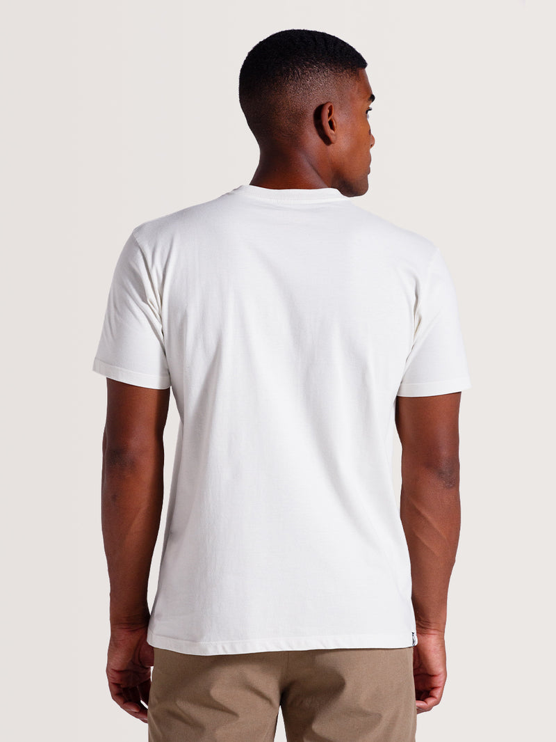 Camiseta cor off white manga curta] com design liso, vista de costas, combinada com calça bege.