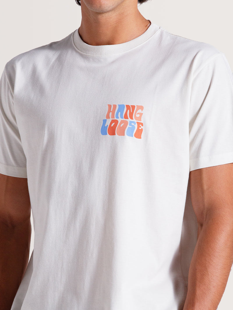 Homem usando camiseta off white básica manga curta com estampa "Hang Loose" estilizada em azul e laranja no lado esquerdo do peito.