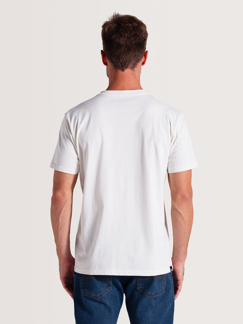 Homem de costas vestindo camiseta off white manga curta, com tecido liso e ajuste reto, combinada com calça jeans azul, sobre fundo claro.