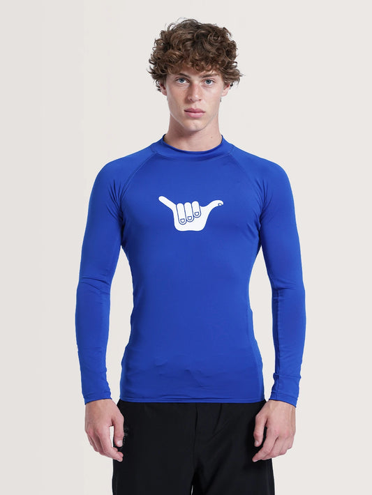 Modelo vestindo camiseta surf manga longa azul. A peça possui arte de mão fazendo sinal Hang Loose na parte frontal.
