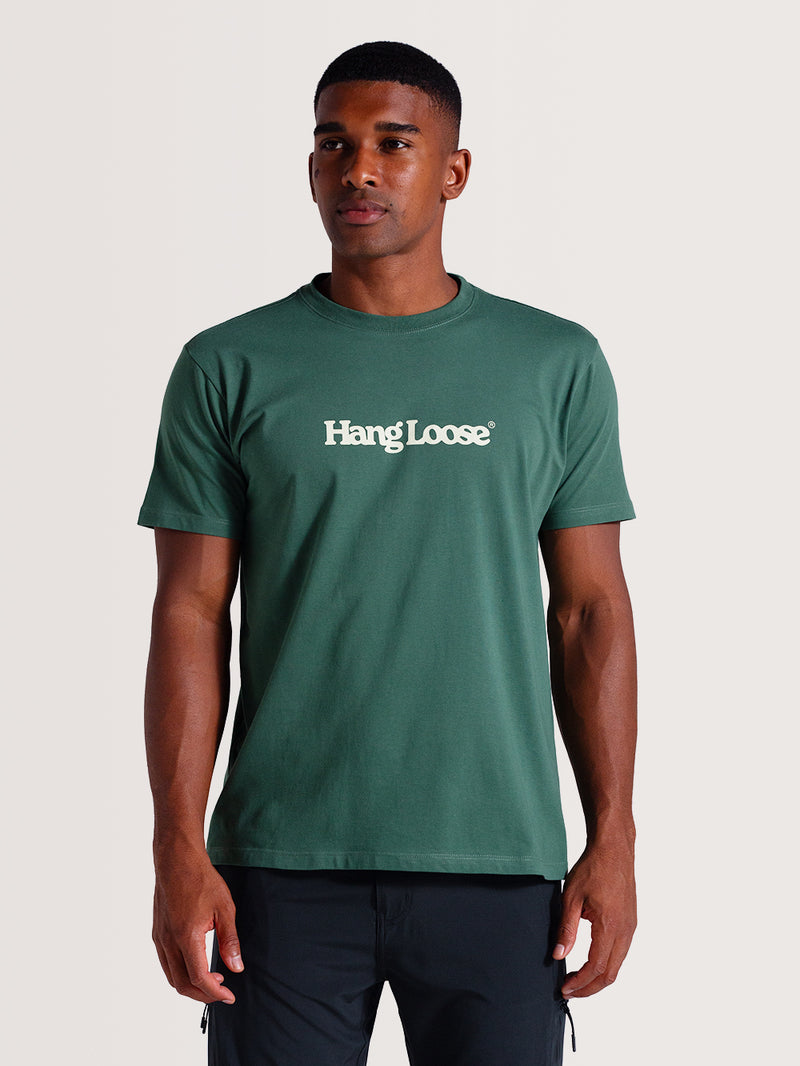 Homem vestindo camiseta verde algodão manga curta com gola redonda e logo "Hang Loose" branco no peito.