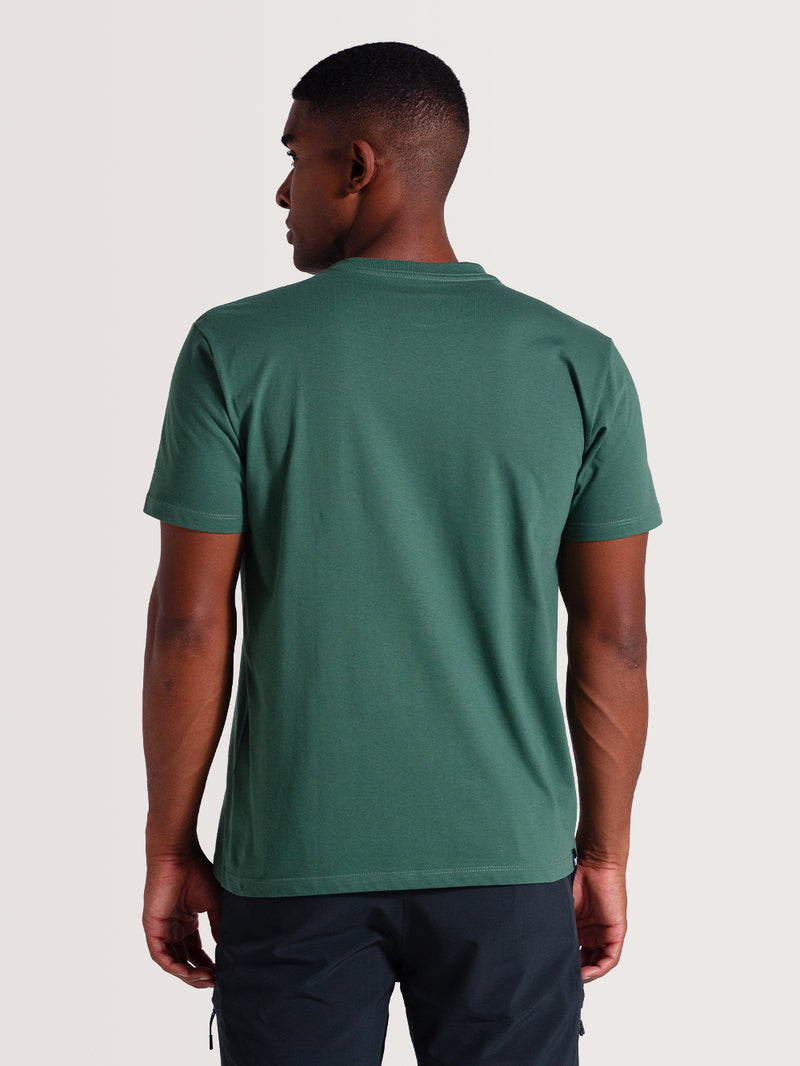Homem de costas vestindo camiseta verde algodão manga curta com gola redonda, combinada com calça escura
