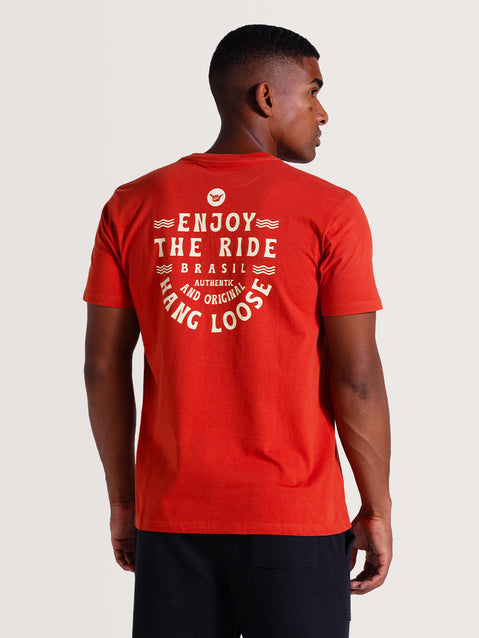 Homem de costas vestindo camiseta vermelha manga curta com estampa branca nas costas que diz "Enjoy The Ride", estilo casual.