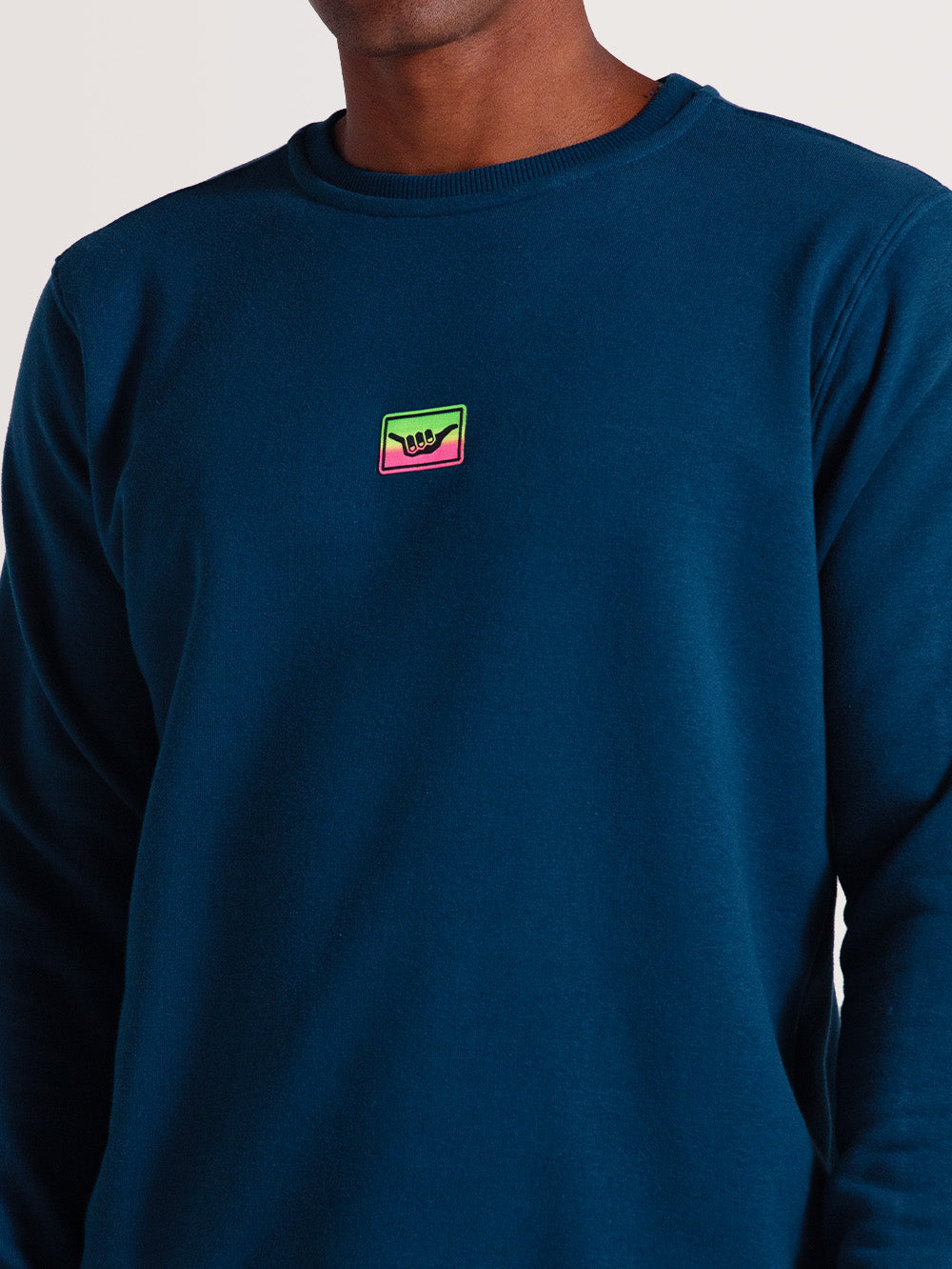 Moletom careca azul em tom escuro, com logo colorido em verde, rosa e amarelo no peito. Corte reto, acabamento simples nos punhos e gola para estilo casual.