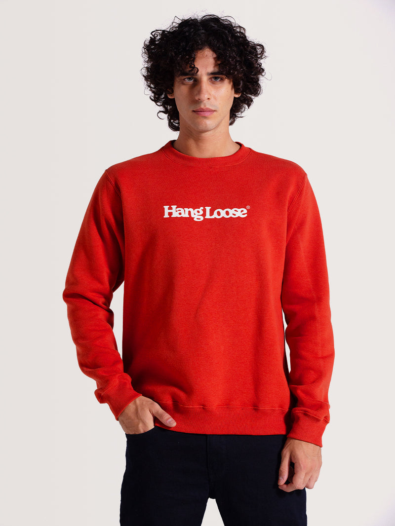 Homem usando moletom careca vermelho felpado com gola redonda e estampa frontal "Hang Loose" em branco. Combina com calça preta casual.