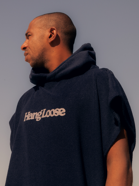 Homem vestindo poncho surf azul marinho com capuz e logo da Hang Loose, ideal para uso após o surfe e momentos ao ar livre.