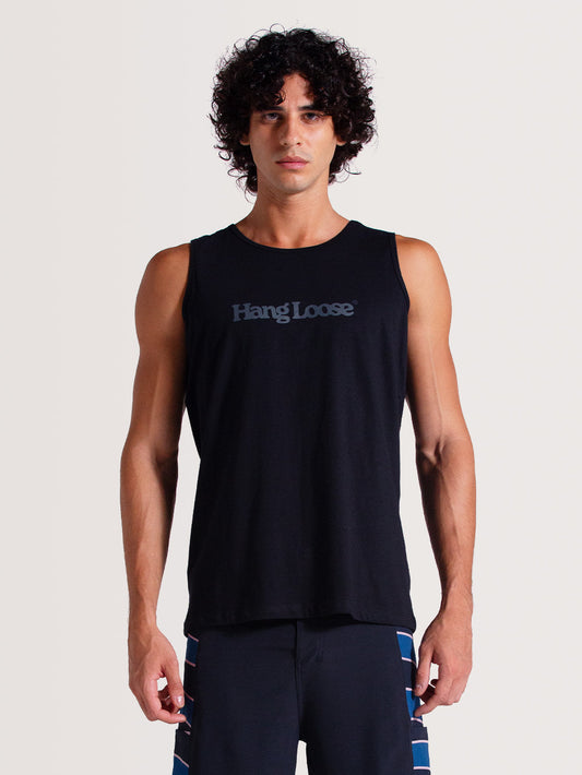Homem vestindo regata preta básica com logo "Hang Loose" estampado em cinza no peito, combinada com bermuda azul com detalhes coloridos, em fundo claro.