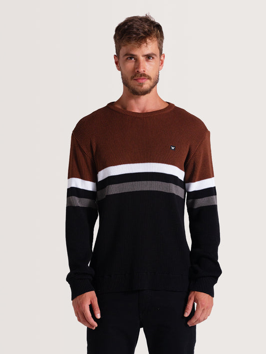 Homem vestindo tricot preto com listras horizontais em branco, cinza e marrom na parte superior. Design casual e elegante, ideal para dias frios.